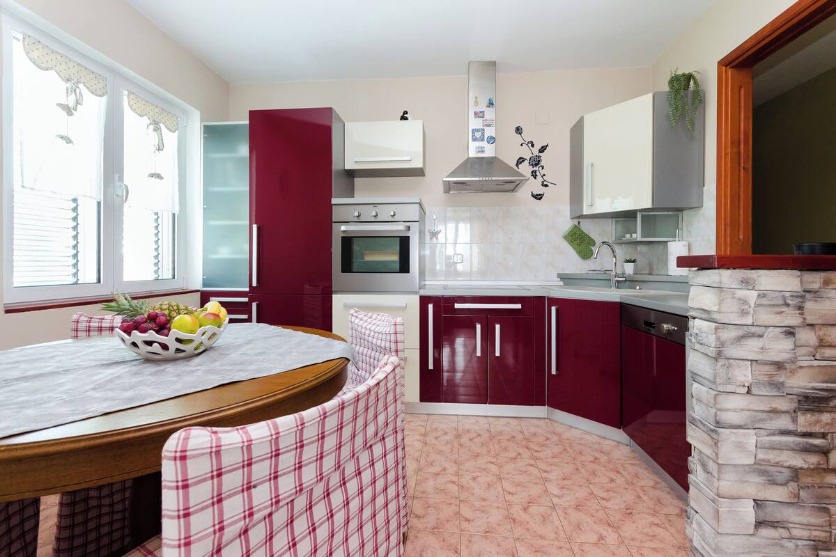 A compact kitchen with a dining area, featuring a stone accent wall, a built-in oven, and a red and white color scheme.