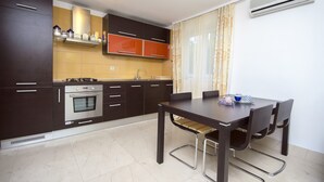 A modern kitchen with dark cabinets, a built-in oven, and a dining table with chairs.
