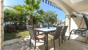 An outdoor patio with a table and chairs, surrounded by greenery and a clear blue sky.