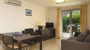 A modern living room with a dining table, sofa, TV, and air conditioning unit.