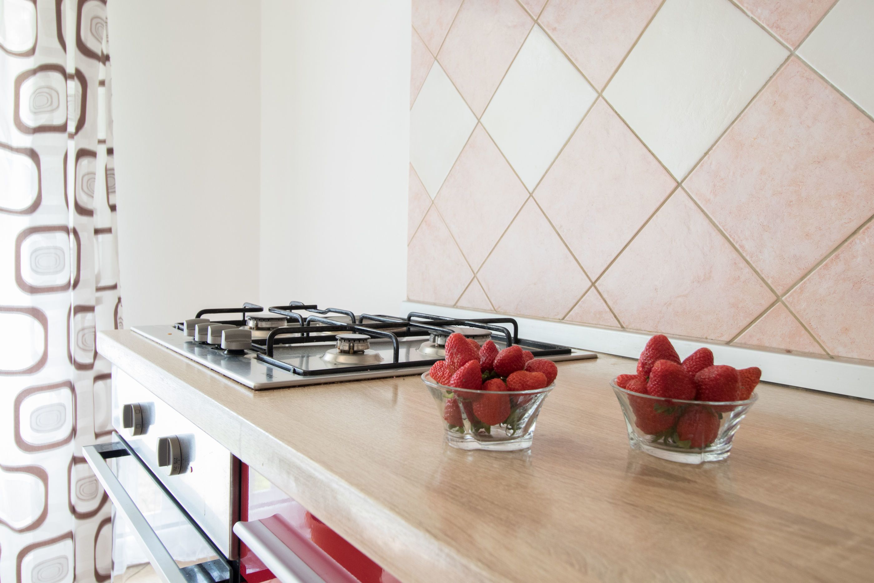 Une cuisine avec un cuisinière à gaz, deux bols en verre remplis de fraises et un mur décoré d’un motif.
