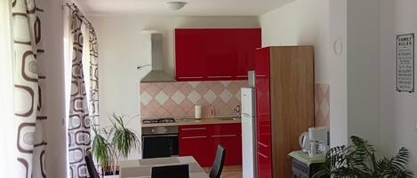 A modern kitchen with red cabinets, a dining area with a table and chairs, and a kitchen island with a sink and stove.