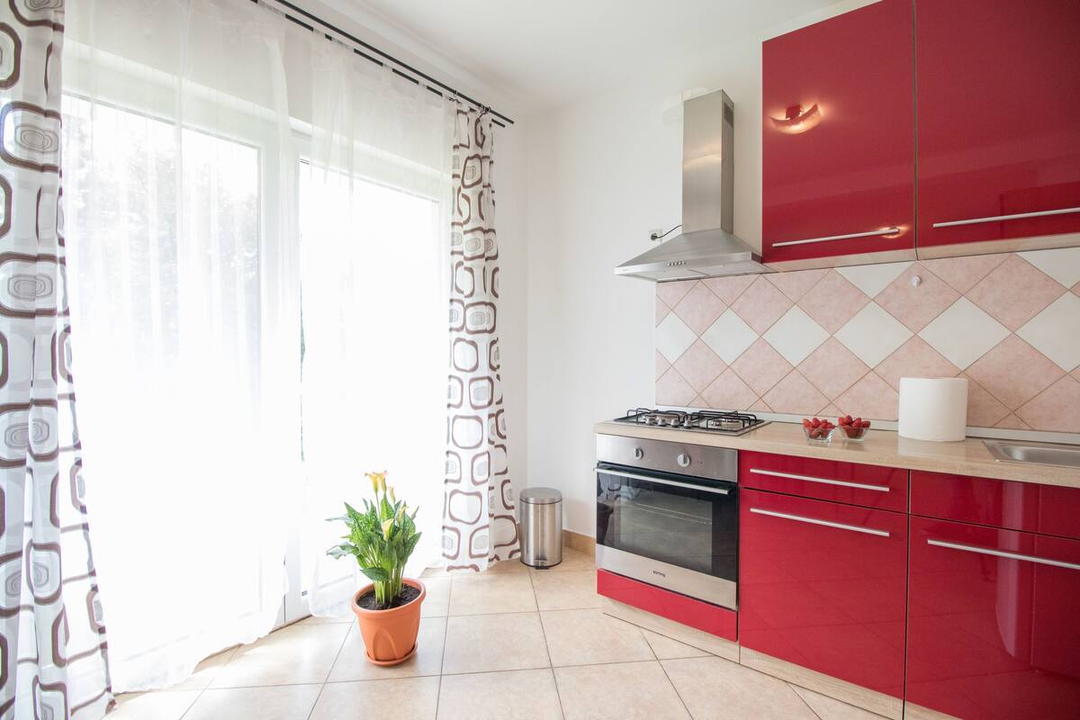 A modern kitchen with red cabinets, a gas stove, and a tiled backsplash.