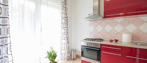 A modern kitchen with red cabinets, a gas stove, and a tiled backsplash.