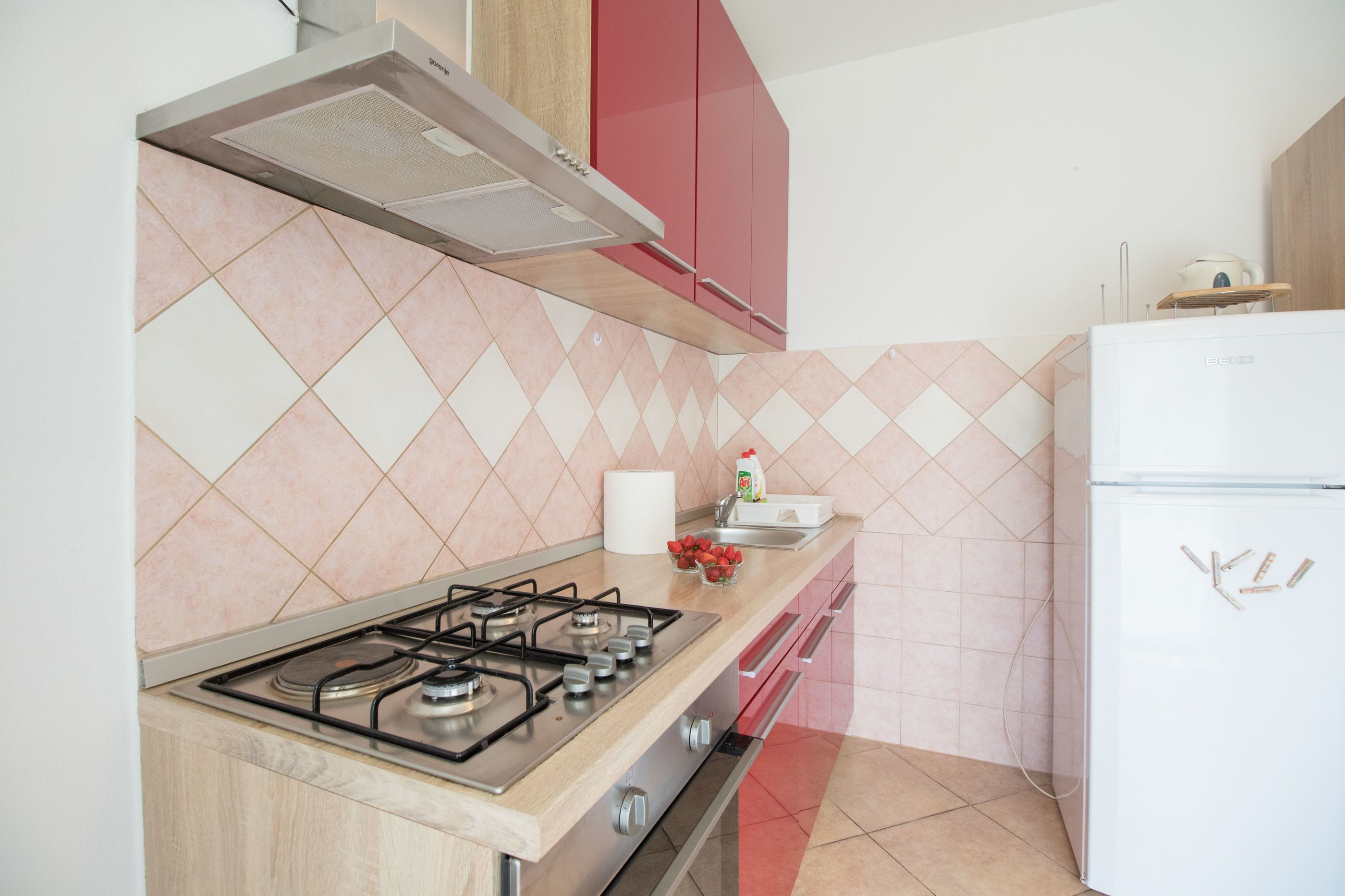 A kitchen with a gas stove, a white refrigerator, and pink and white patterned tiles.