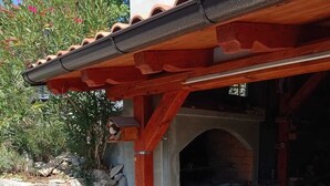 Eine Steinsäule, ein Blumentopf und ein Backofen aus Ziegelsteinen unter einem roten Dach.