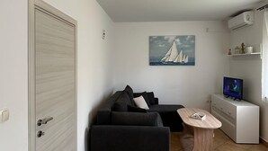Ein gemütlicher Wohnraum mit einer Couch, einem Couchtisch, einem Fernseher und einem Segelboot-Bild an der Wand.