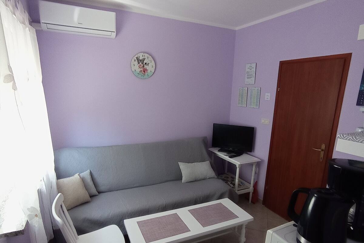 A living room with a sofa, a coffee table, a television, and a kettle.