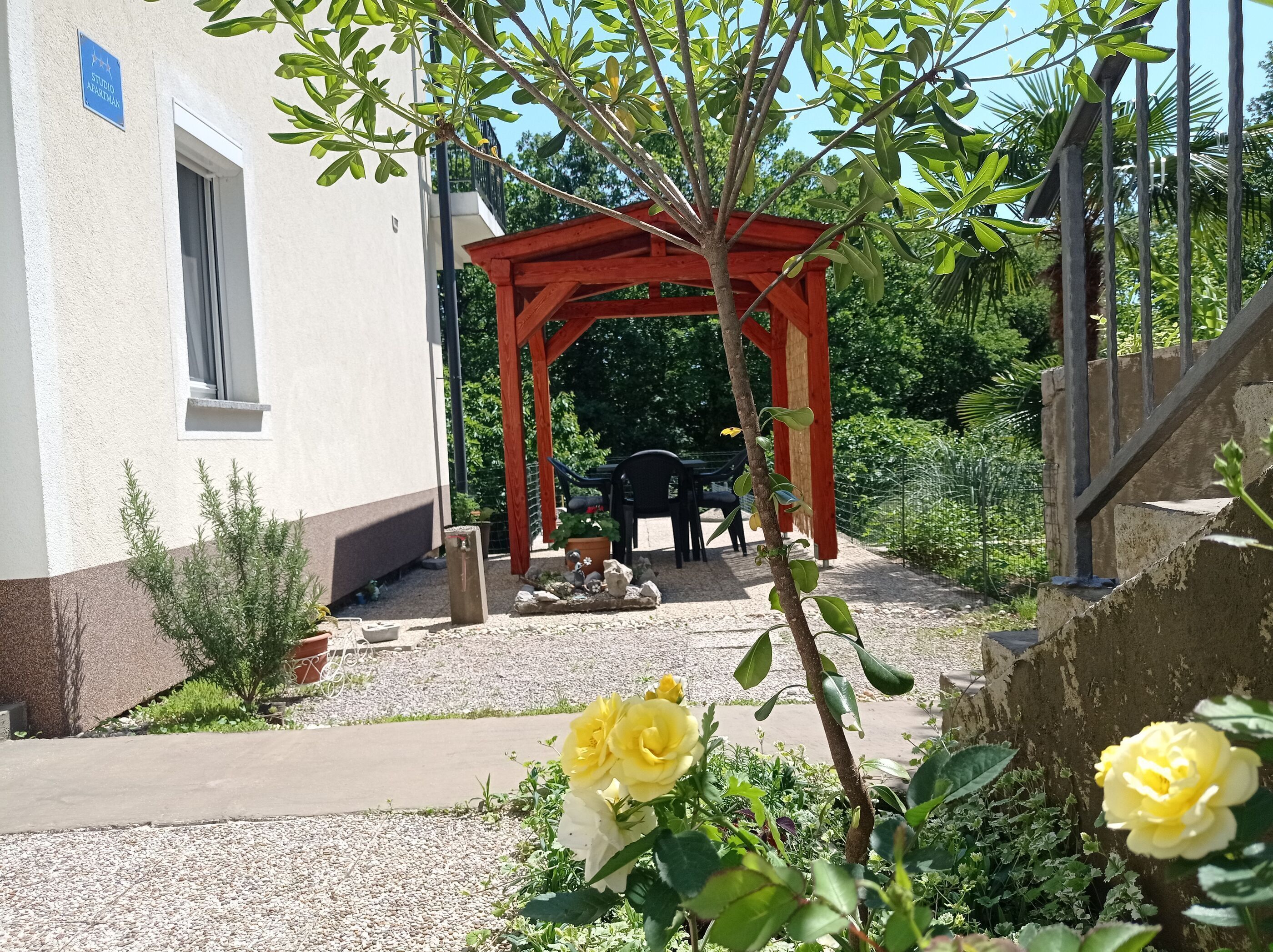 Un jardín con un porche de madera, una mesa y sillas, y rosales amarillos.
