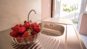 Ein Spülbecken mit Armatur aus Edelstahl und eine Schale frische Erdbeeren auf der Arbeitsfläche.