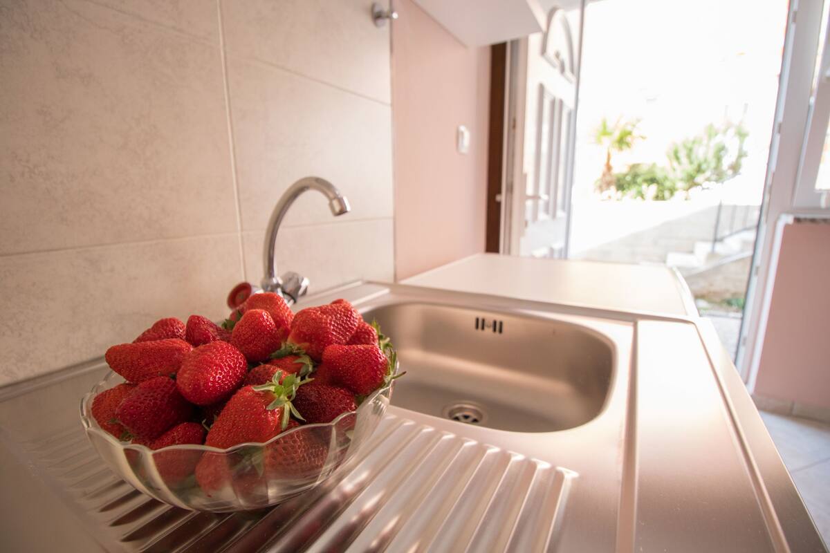 A kitchen sink with a stainless steel faucet and a bowl of fresh strawberries on the counter.