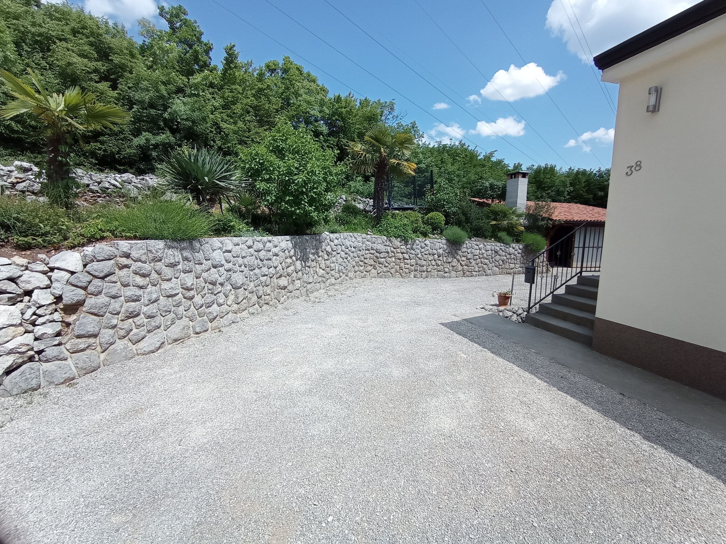 Un camino de grava que conduce a una casa con un muro de piedra y una reja de metal.