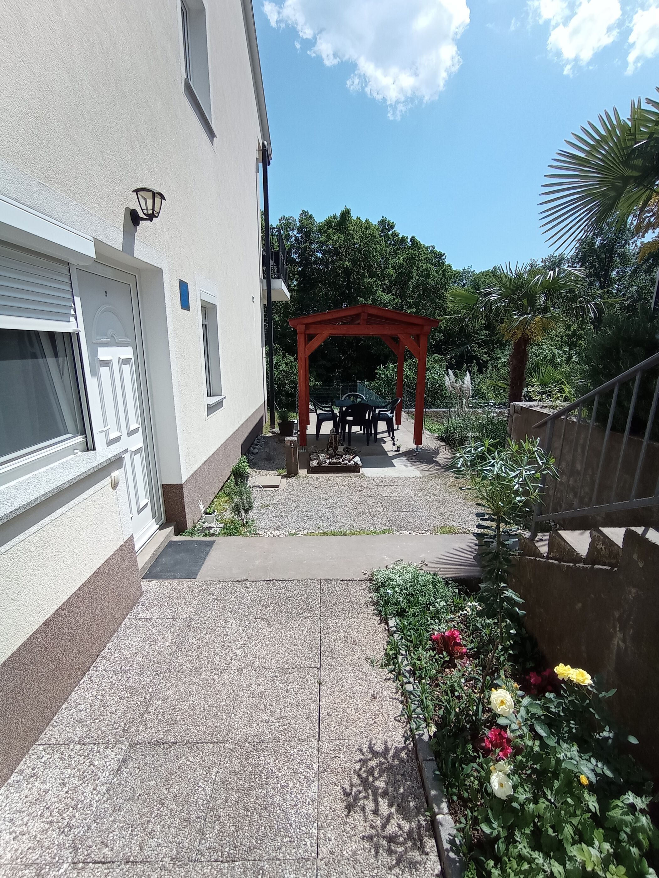 Une cour avec une pergola rouge, un espace aménagé pour s’asseoir et un parterre de fleurs.