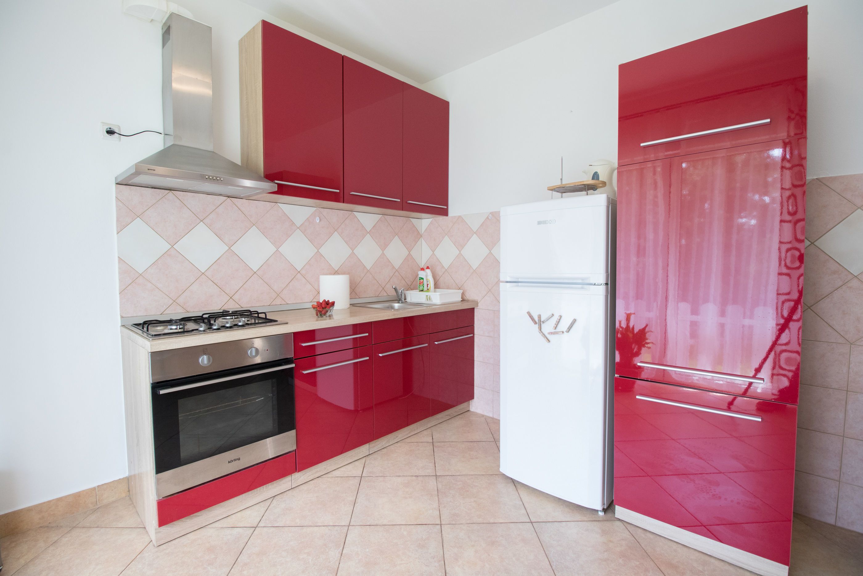 Una cocina con armarios rojos, una estufa de acero inoxidable y un refrigerador blanco.