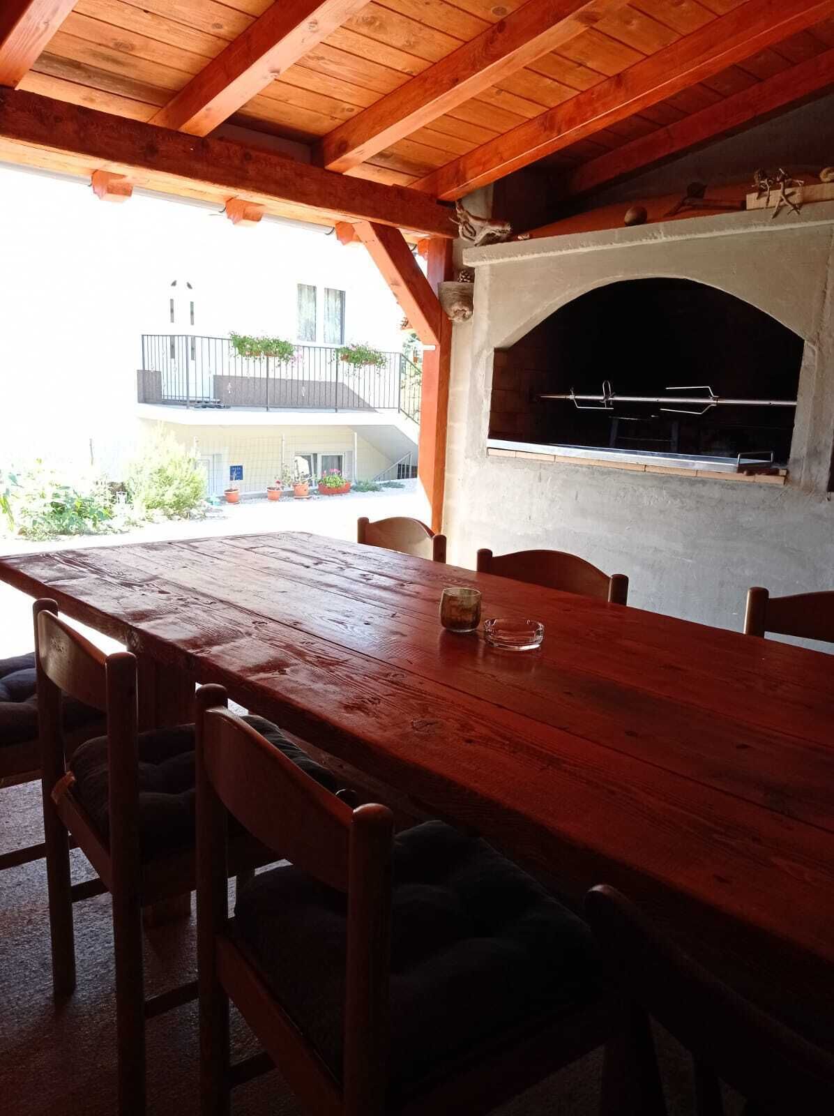 Ein Holzespeisetisch mit Stühlen, eine Terrassenveranda und ein Kamin aus Stein.