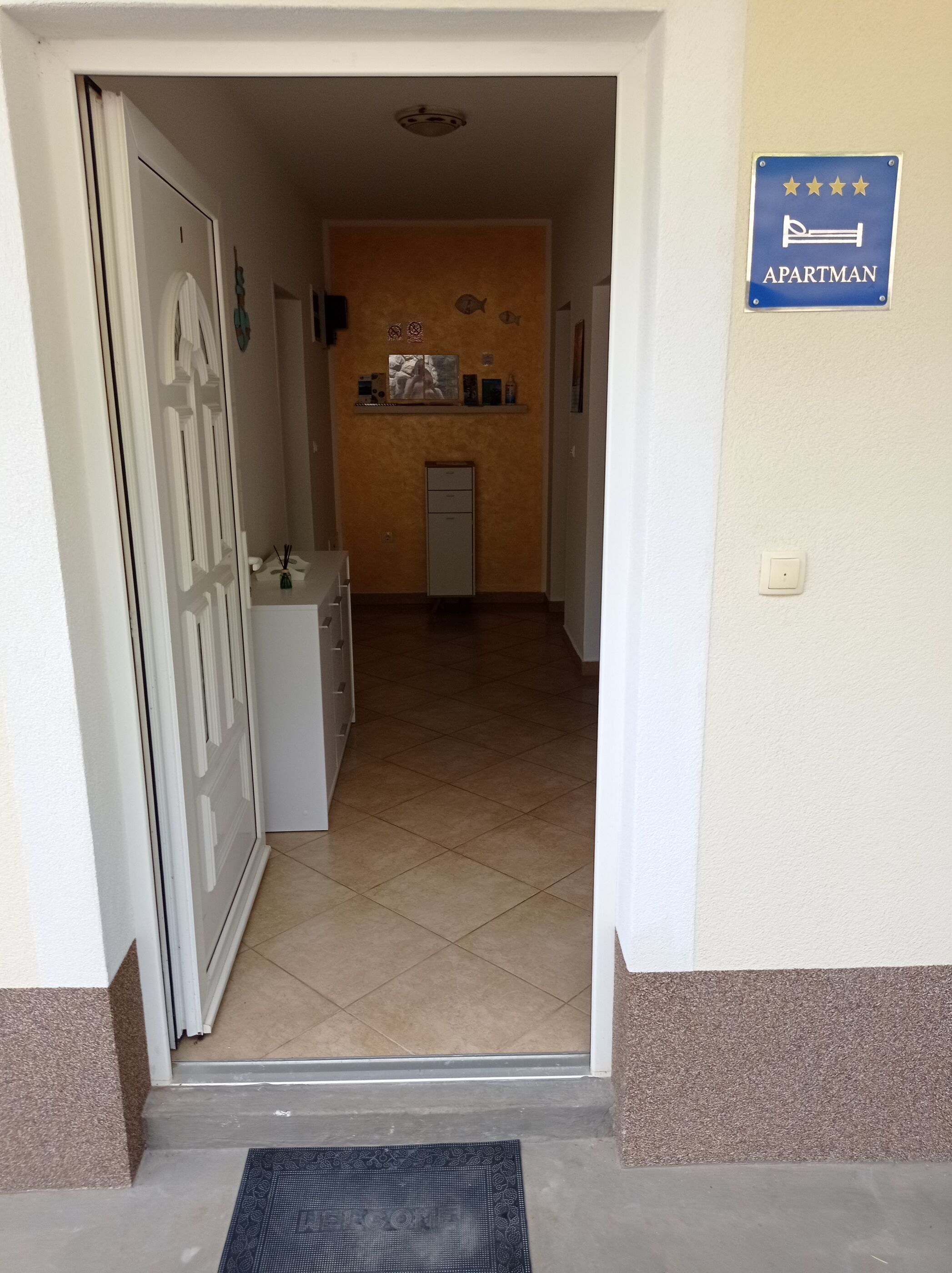 A hallway leading to an apartment with a tiled floor, a small refrigerator, and a sign indicating it is an apartment.