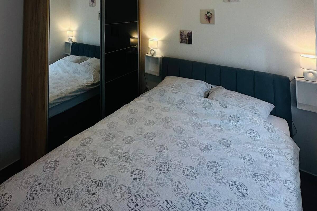 A bedroom with a bed, a wardrobe, a nightstand, and a wall-mounted light fixture.