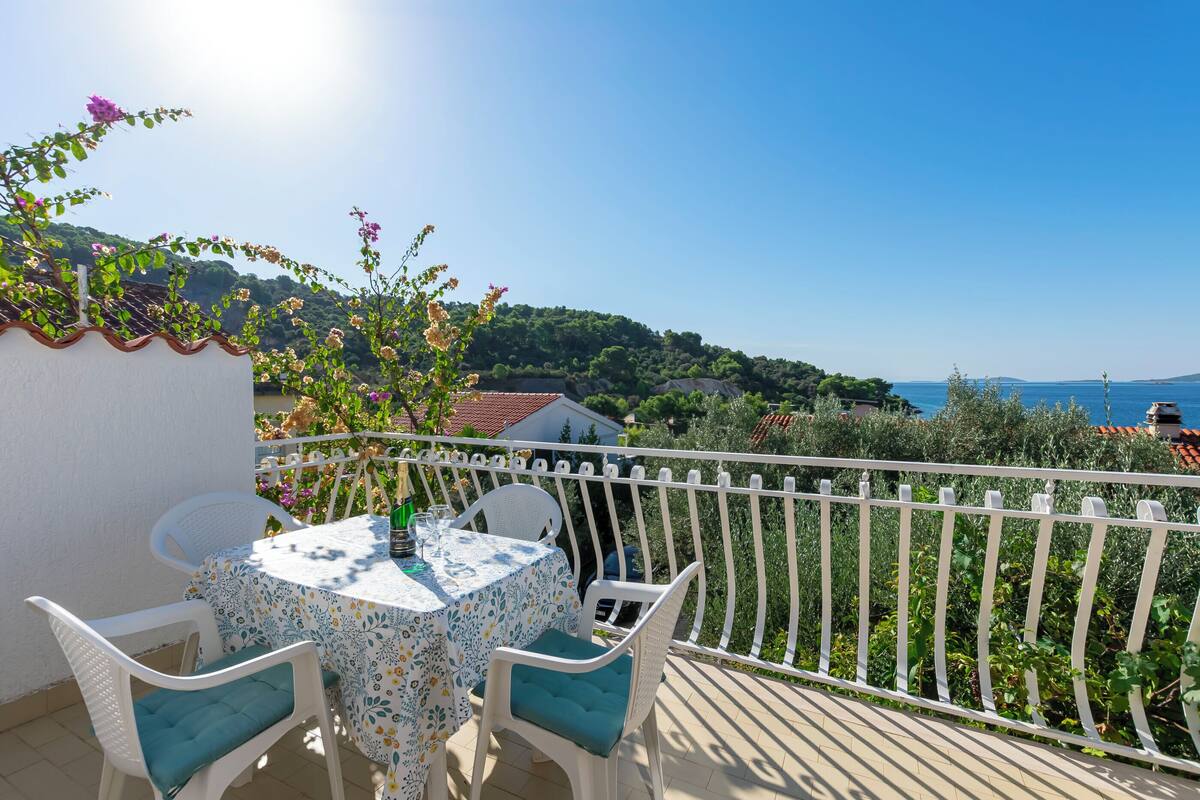 Un balcone con tavolo e sedie, affacciato su un paesaggio suggestivo con colline e un corpo d'acqua.
