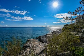 Une vue sur la côte, avec un ciel dégagé, un rivage rocheux et un bâtiment doté d’un balcon donnant sur la mer.