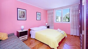 A room with pink walls, a bed with a yellow bedspread, a nightstand with a lamp, and a window with curtains. - Apartments Mise (Makarska)