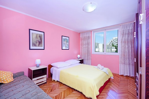 A room with pink walls, a bed with a yellow bedspread, a nightstand with a lamp, and a window with curtains.