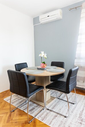 A round table with black chairs, a small vase with flowers, and an air conditioning unit on the wall. - Apartments Marinko (Makarska)