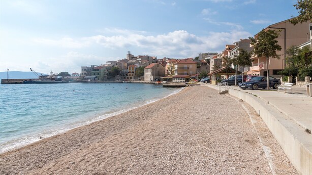 Un pueblo costero con playa de guijarros, edificios a lo largo de la costa y cielo despejado.
