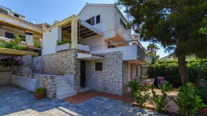 A two-story house with a stone facade, a balcony, and a small patio area with outdoor furniture. - Apartment Natasa (Okrug Gornji)