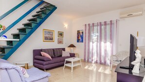 A living room with a purple sofa, a white coffee table, a staircase with blue railings, and a white chair. - Apartment Natasa (Okrug Gornji)