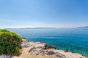 Ein Küstenblick mit klarem, blauem Wasser, felsigem Gelände und einem Weg zum Meer.