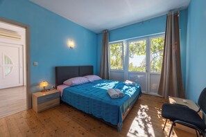 A bedroom with a bed, bedside table, chair, and a window with curtains.
