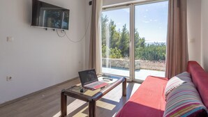 Una habitación con una computadora portátil sobre una mesa de vidrio, un televisor montado en la pared y un sofá con un cojín a rayas.