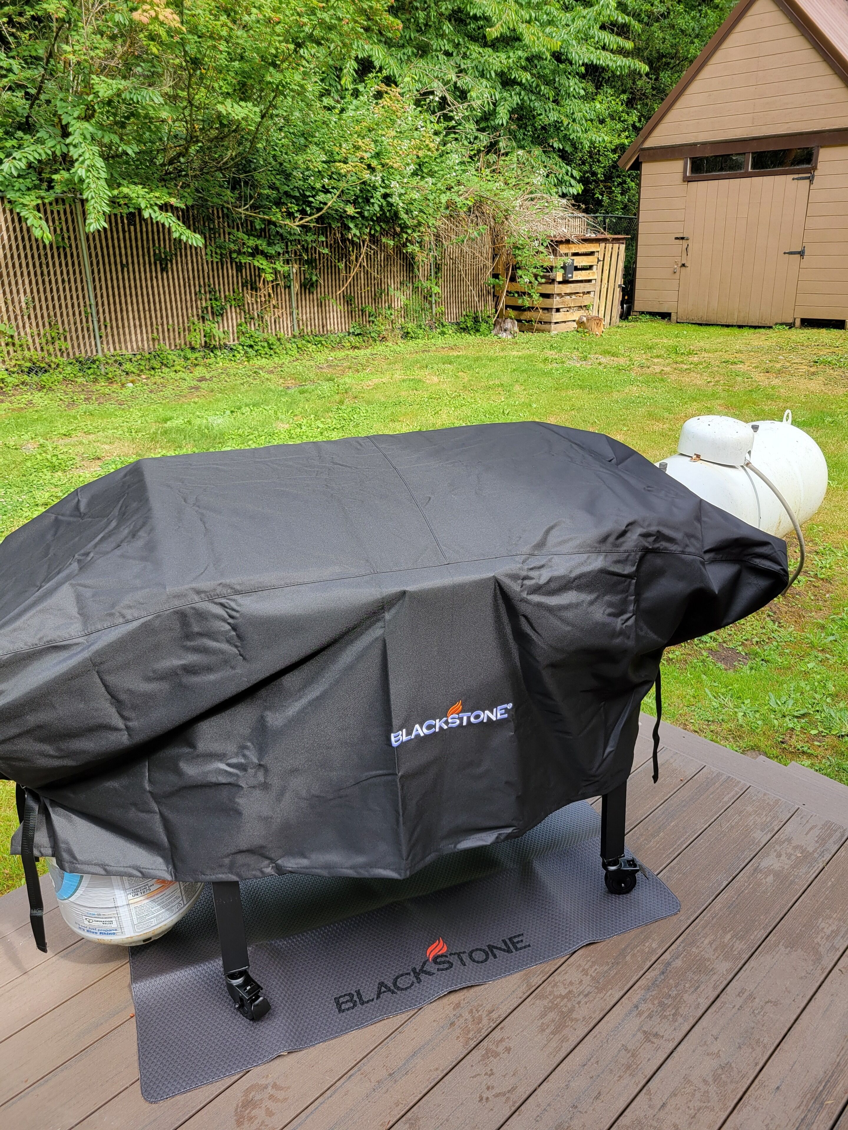 Una parrilla para barbacoa cubierta con una funda Blackstone sobre una terraza de madera.