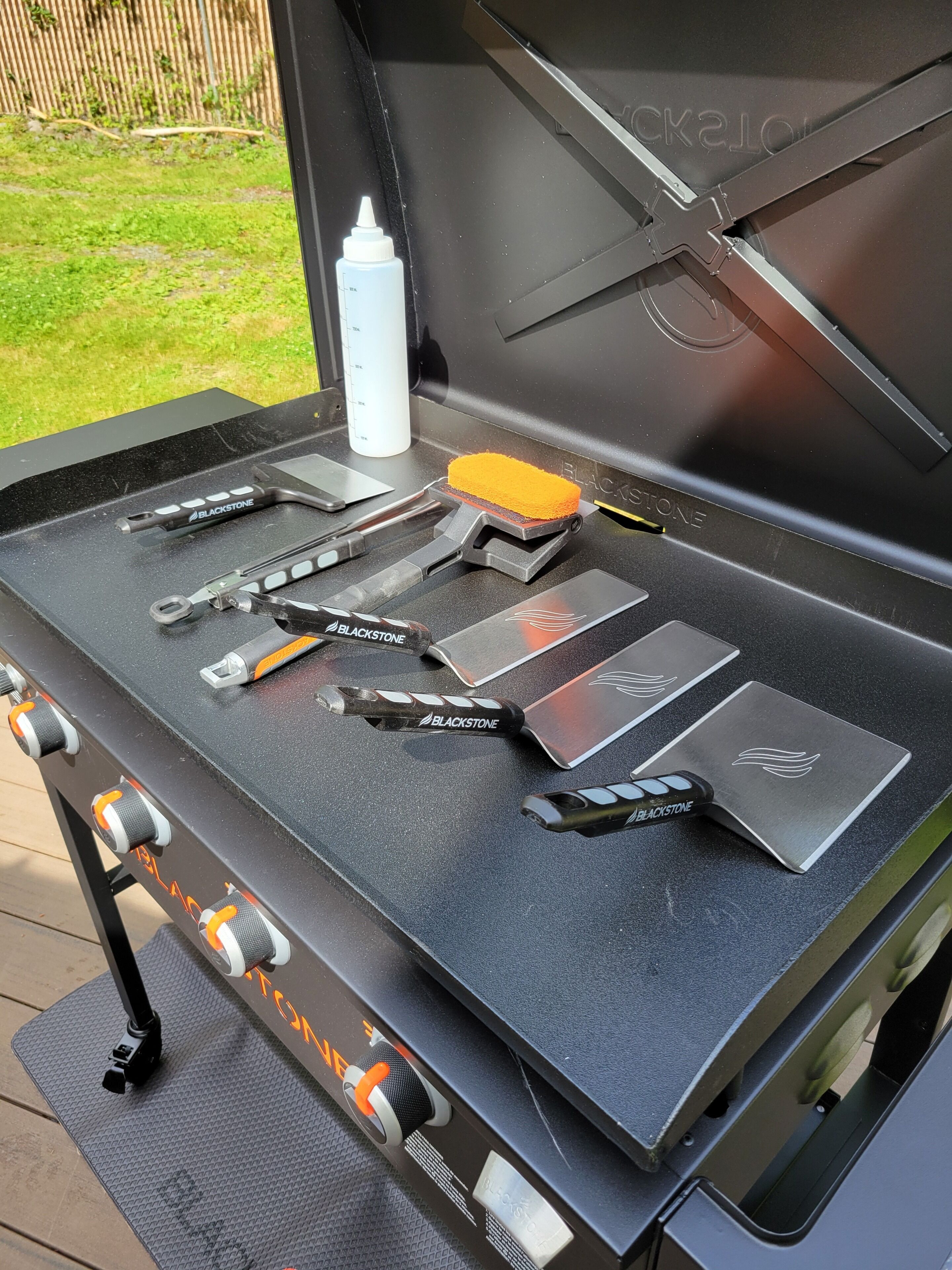 Un barbecue avec les ustensiles et une bouteille posés sur le plan de travail.