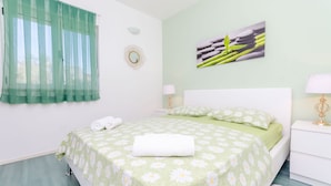 Un lit bien fait, recouvert d’une courtepointe à motifs floraux verts, avec un oreiller blanc et une serviette blanche roulée posée sur le côté.