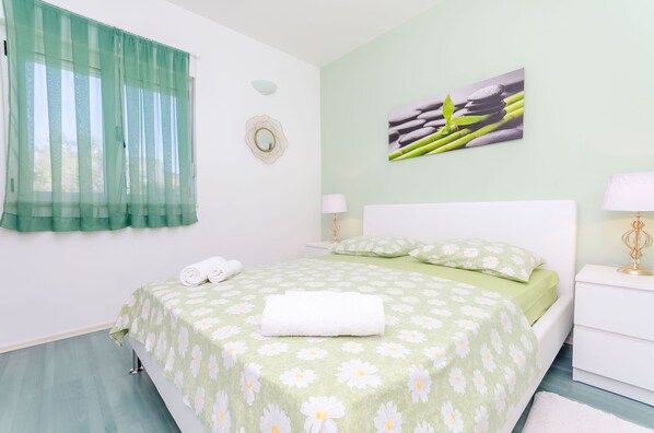 A neatly made bed with a green floral bedspread, a white pillow, and a rolled white towel on the side. - Apartments Zdenka (Okrug Donji)