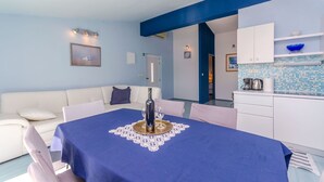 Un coin repas avec une table dressée pour deux personnes, un canapé blanc et un espace cuisine avec un revêtement mural bleu.