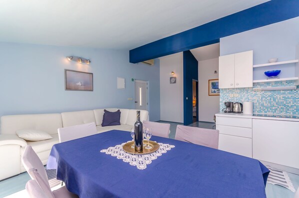 Un coin repas avec une table dressée pour deux personnes, un canapé blanc et un espace cuisine avec un revêtement mural bleu.