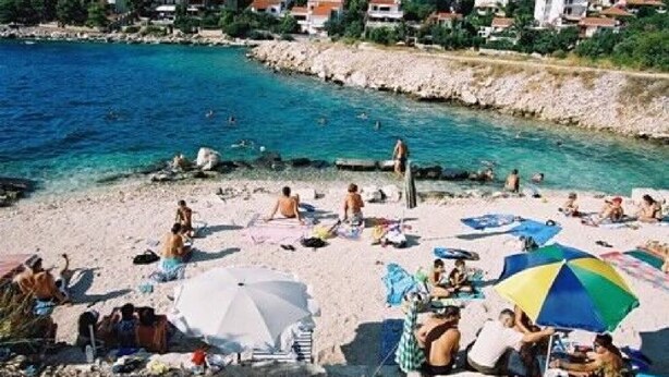 Une plage où l’on peut voir des gens se prélasser au soleil et se baigner, des parasols et une côte rocheuse.