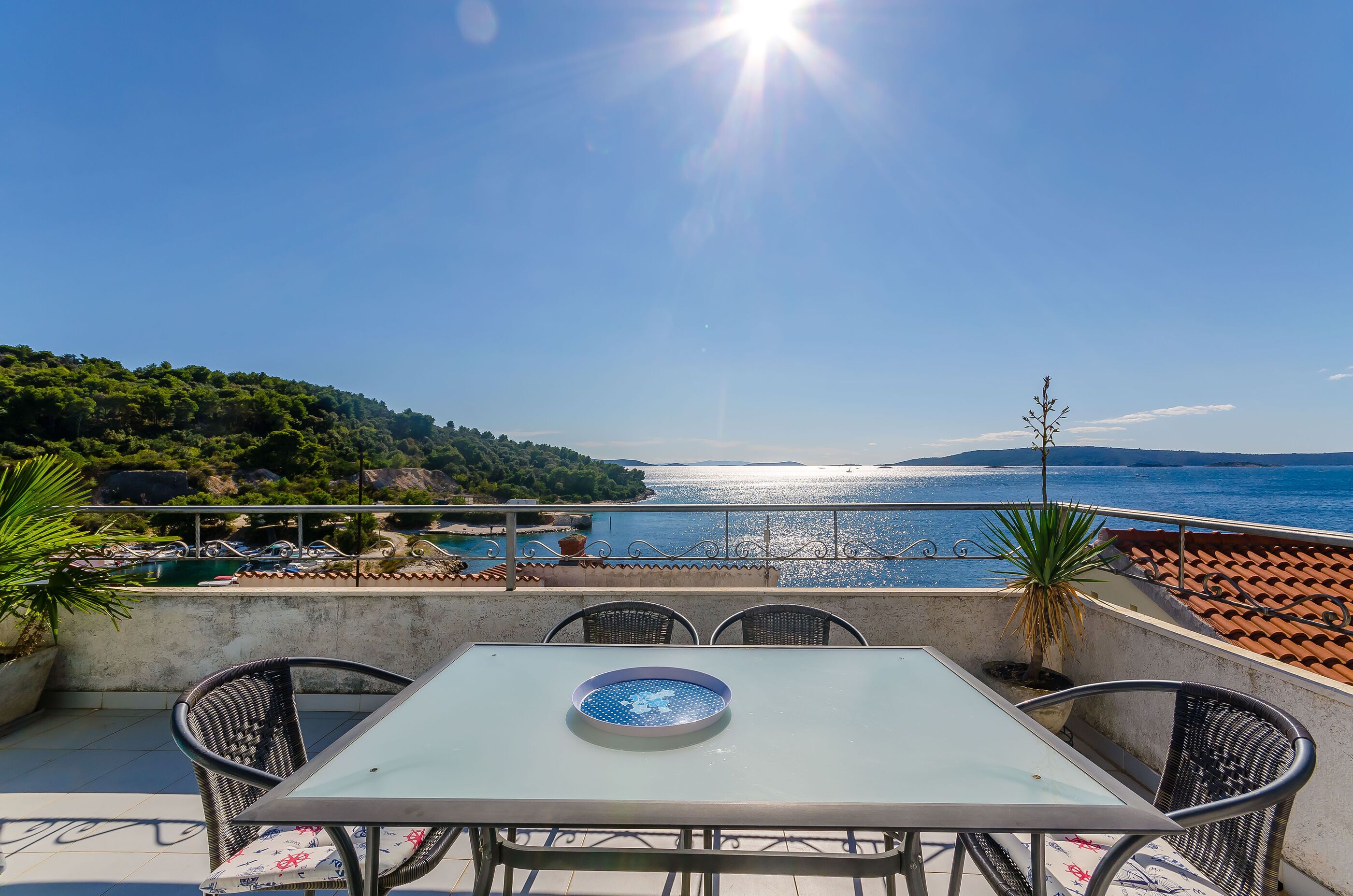 A terrace with a table and chairs, overlooking a coastal view with a clear sky.