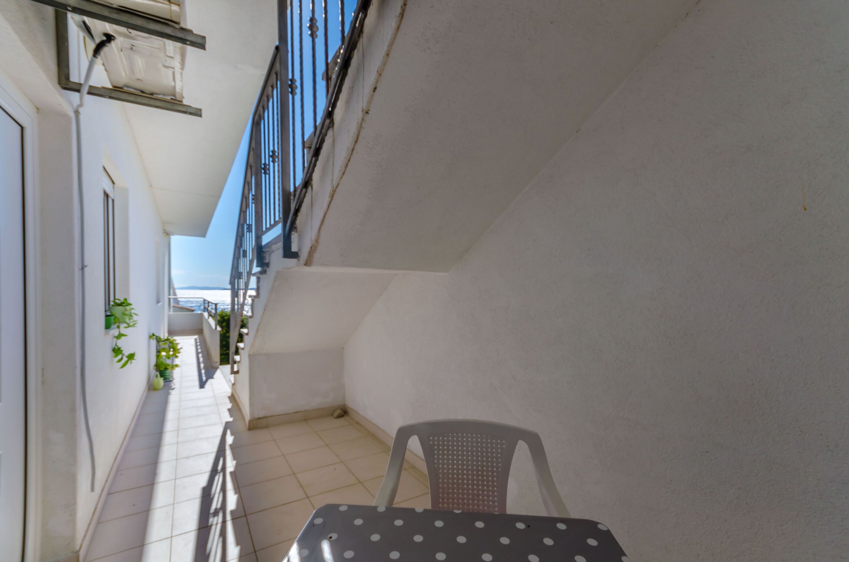 Un petit balcon avec une table et une chaise, un sol carrelé et des plantes en pot.