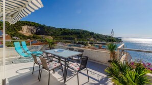 Une terrasse avec une table et des chaises, offrant une vue sur la côte, avec une piscine et de la verdure.