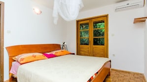 Un dormitorio con una cama de madera, una mesita de noche, un ventanal con vistas a la vegetación y un equipo de aire acondicionado.