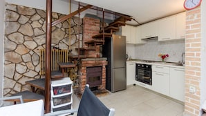 Una cocina compacta con pared de piedra, chimenea de ladrillo, refrigerador de acero inoxidable y un pequeño comedor con mesa y sillas.
