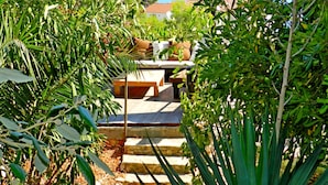 Una escalera conduce a un área de estar al aire libre techada, con vista a un edificio de tejas rojas.