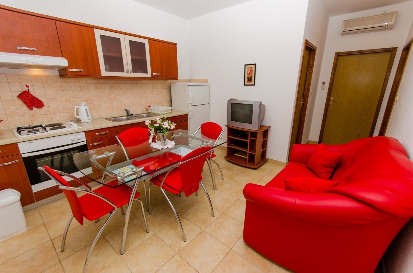 A compact kitchen with a dining area, a red sofa, and a television.