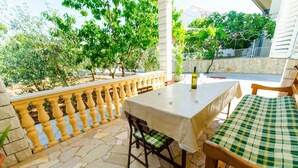 An outdoor patio with a table set for dining, surrounded by stone flooring and a yellow balustrade. - Apartments Ivana (Trogir)