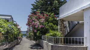 A narrow street with a white building on the right, a stone wall, and a metal railing. - Apartment Maslina (Vodice)
