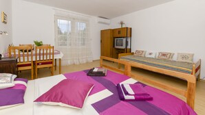 A bedroom with a bed, a wooden chair, a small table, a TV, and a window with curtains. - Apartment Maslina (Vodice)