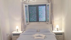 A bedroom with a large bed, two bedside tables with lamps, a chandelier, and a window with blinds. - Apartments Damir - Katarina (Sutivan)